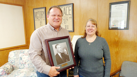 Photo by Mike Steely.  Butch Inman of Dott Baker Insurance Agency holds a photo of his grandfather, the founder of the company. Teri Huskey, Customer Service Manager, joined Inman for the photo. 